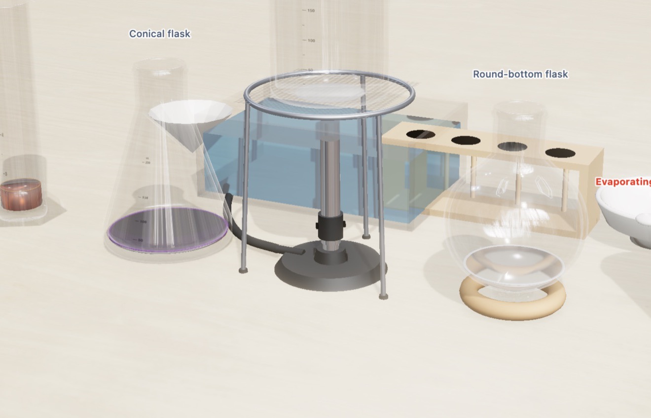 The Bench, the chemistry lab table: permanganate in a conical flask, iron(III) chloride in a measuring cylinder, a round bottom flask in its ring, a trough, a rack, a funnel and a lit Bunsen burner on a birch bench